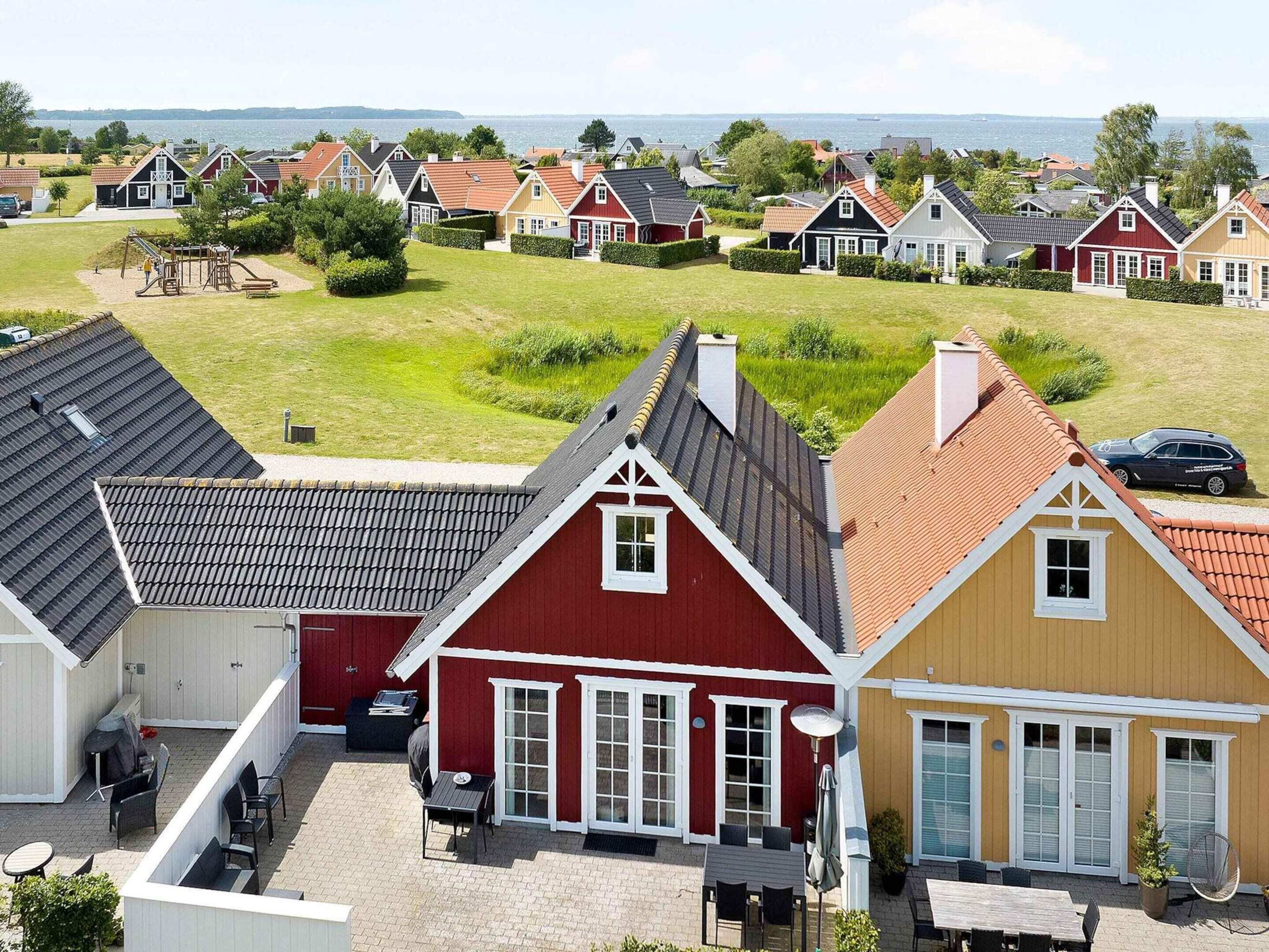 Una hilera de casas tradicionales con fachadas rojas y amarillas, un área verde y vista al mar.