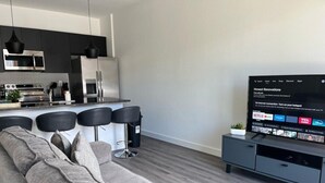 A modern living room with a grey sofa, a TV, and a kitchen area with dark cabinets and stainless steel appliances. - 3 bedrooms house 12 minutes to Disney (Kissimmee)