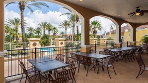 Une terrasse extérieure avec des tables et des chaises, une piscine et des palmiers.