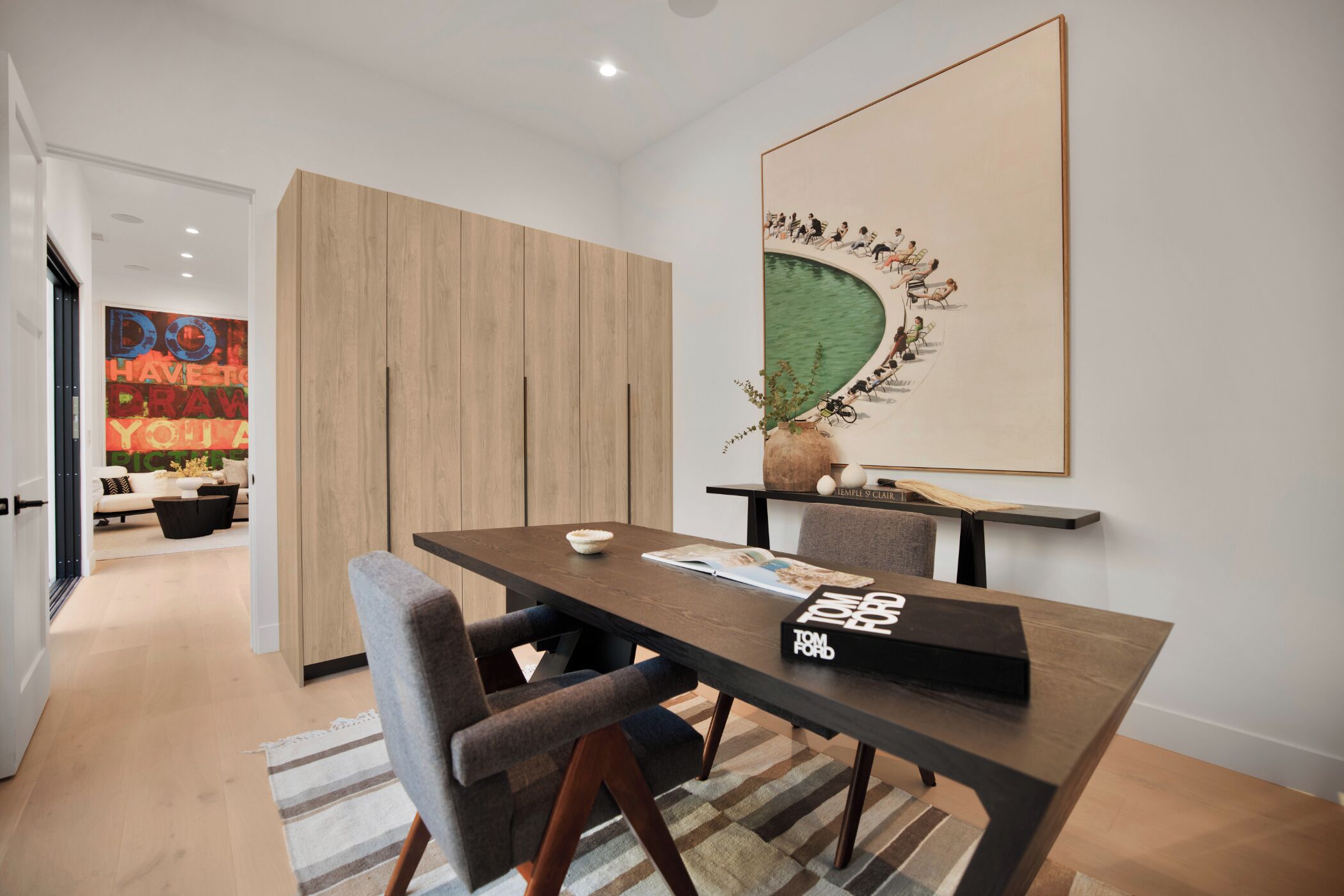 A modern dining area with a wooden table, grey upholstered chairs, and a framed artwork above.