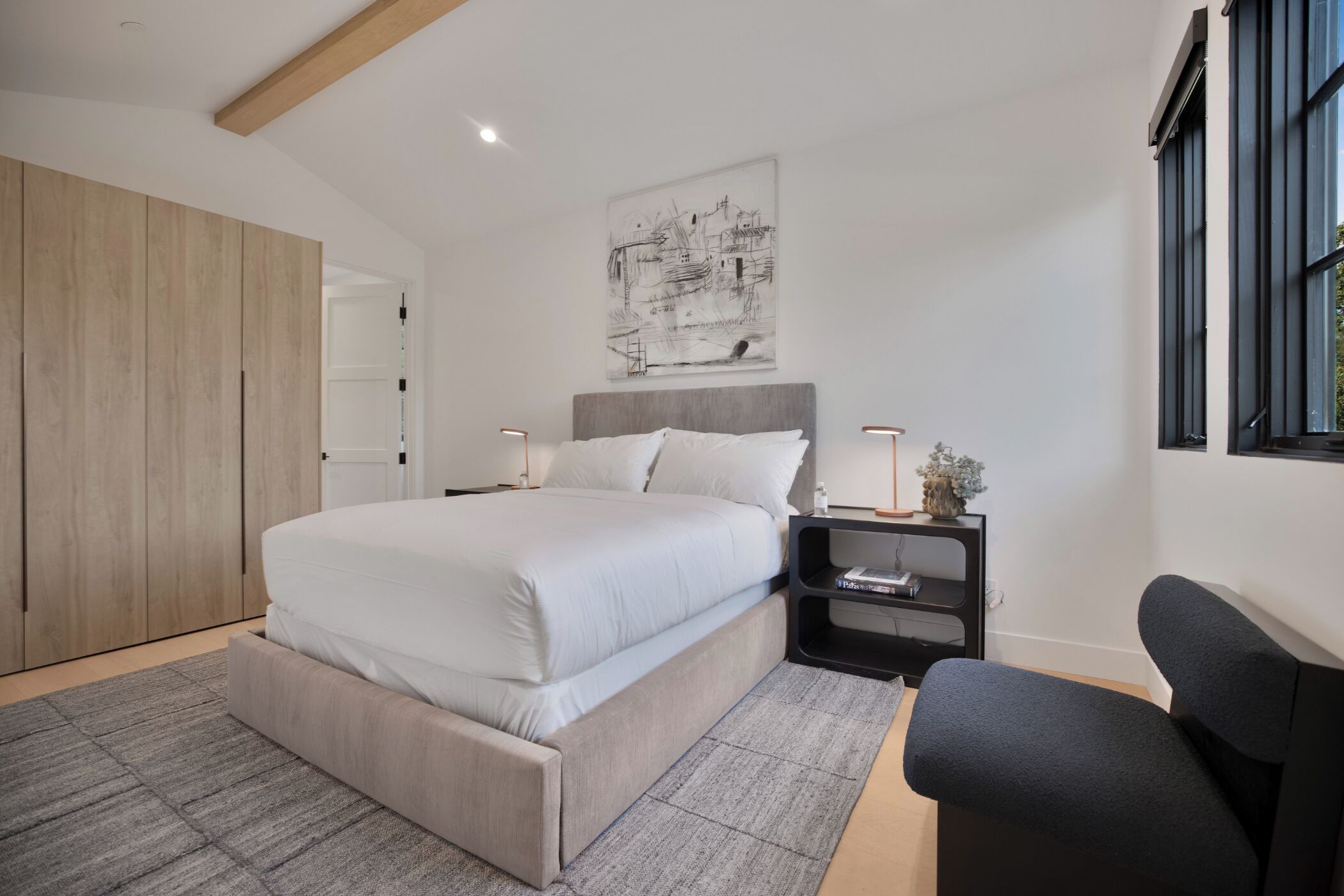 Um quarto moderno com uma cama grande, uma mesa de cabeceira com abajur, uma cadeira e um quadro na parede.