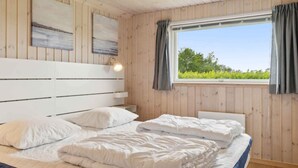 Ein Schlafzimmer mit hölzernem Kopfteil, zwei Betten, einem Fenster mit Vorhängen und einem Bild an der Wand.