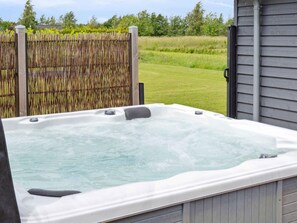 Un bain à remous en plein air, entouré d’une clôture en bois, avec un champ verdoyant en arrière-plan.