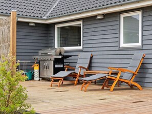 Une terrasse avec un barbecue, deux fauteuils de jardin en bois et une fenêtre donnant sur la plateforme.