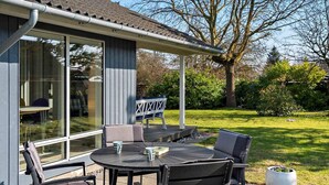 An outdoor patio with a round table and chairs, a covered seating area, and a view of the surrounding garden. - 5 Star Holiday Home in Vordingborg (Vordingborg)