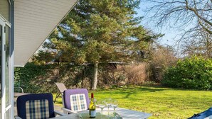 A deck with a table set for two, outdoor seating, and a view of the surrounding garden. - 5 Star Holiday Home in Vordingborg (Vordingborg)