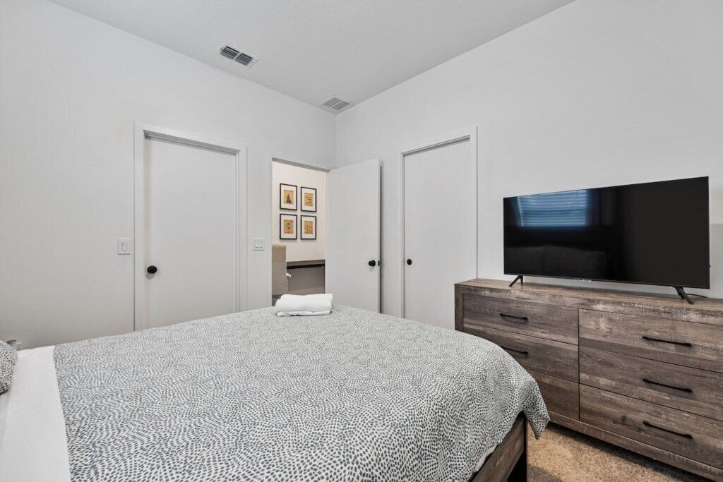 Une chambre à coucher avec un lit, un téléviseur posé sur une commode en bois, et une porte donnant accès à une salle de bain.