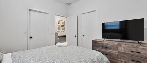 Une chambre à coucher avec un lit, un téléviseur posé sur une commode en bois, et une porte donnant accès à une salle de bain.