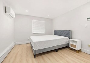 A bedroom with a bed, bedside table, and a wall-mounted air conditioning unit. - Renovated 2-Bedroom in Sylvan Beach / Furnished + Laundry / Monthly (Blossvale)