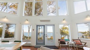 A spacious room with large windows offering views of the sea and trees. - Owl's Landing: Bright 3-Bed Coastal Home with Loft, Screen Room & Ocean Views (Prince Edward Island)