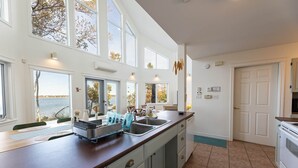 A kitchen with a large island, multiple windows, and a view of the outdoors. - Owl's Landing: Bright 3-Bed Coastal Home with Loft, Screen Room & Ocean Views (Prince Edward Island)