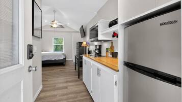 A compact kitchen with white cabinets, a wooden countertop, and a built-in refrigerator.