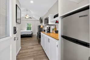 A compact kitchen with white cabinets, a wooden countertop, and a built-in refrigerator.