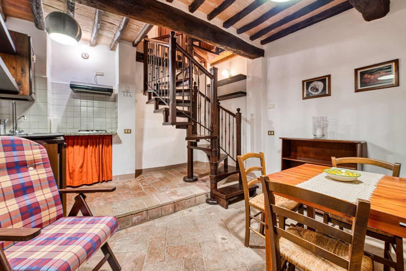 A kitchen with a wooden staircase, a dining table with chairs, and a plaid chair.
