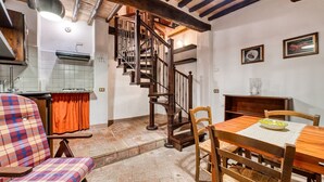 A kitchen with a wooden staircase, a dining table with chairs, and a plaid chair. - GuestHost - Comfortable apartment of approximately 45 square meters, perfect for a stay of two, located on the ground floor of a period building (accessible via a few steps).The property is located in Bagnaia, a quiet hamlet a few kilometers from Perugia (Bagnaia)