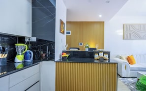 A modern kitchen with a black countertop, a wooden island, and a white sofa in the living area.