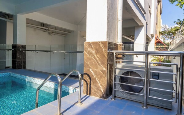 Una piscina con agua cristalina, rodeada por un solado de baldosas y barandales de metal.