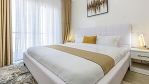 Una habitación de hotel con una cama grande, una mesita de noche con lámpara y una ventana con cortinas.