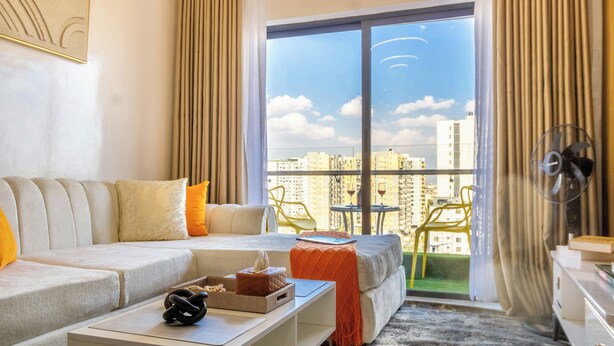 Un salón moderno con un sofá, una mesa de centro y vistas de la ciudad a través de grandes ventanales.