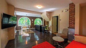 A spacious living area with a flat-screen TV mounted on the wall, a dining area with a table and chairs, and a red sofa. - Stylish 1 bedroom ap in downtown (Antigonish)
