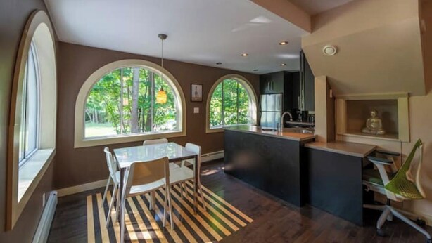 A modern kitchen with a dining area, large windows, and a view of greenery. - Stylish 1 bedroom ap in downtown (Antigonish)