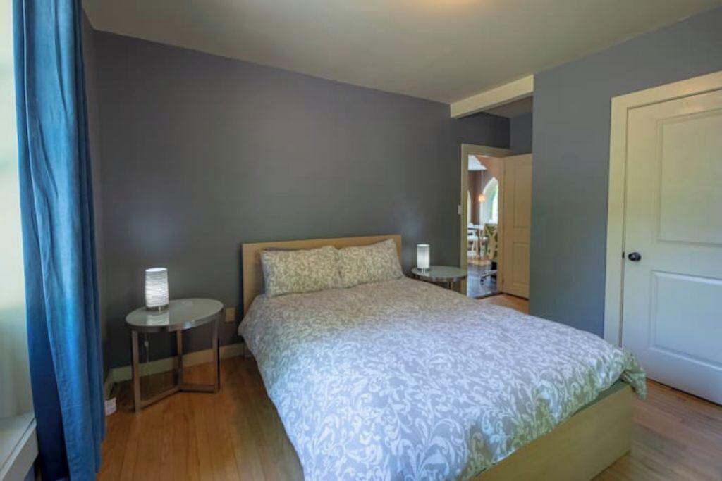 Ein Schlafzimmer mit einem Bett, einem Nachttisch, einer Lampe und einer Tür.