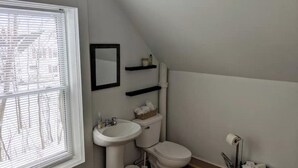 Ein kleines, sauberes Badezimmer mit Toilette, Waschbecken und Regalen.