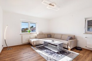 Un salon moderne avec un canapé, une table basse, un lampadaire et une vue sur l’extérieur.