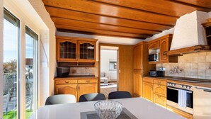 A kitchen with wooden cabinets, a dining table with chairs, and a view of the outdoors. - Attic Apartment with Air Conditioning in Freilassing (Freilassing)