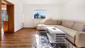 A modern living room with a sofa, a coffee table, and a window with a view of a building. - Attic Apartment with Air Conditioning in Freilassing (Freilassing)