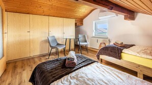 Een kamer met houten balkenplafond, een bed, een stoel, een klein tafeltje en een raam.