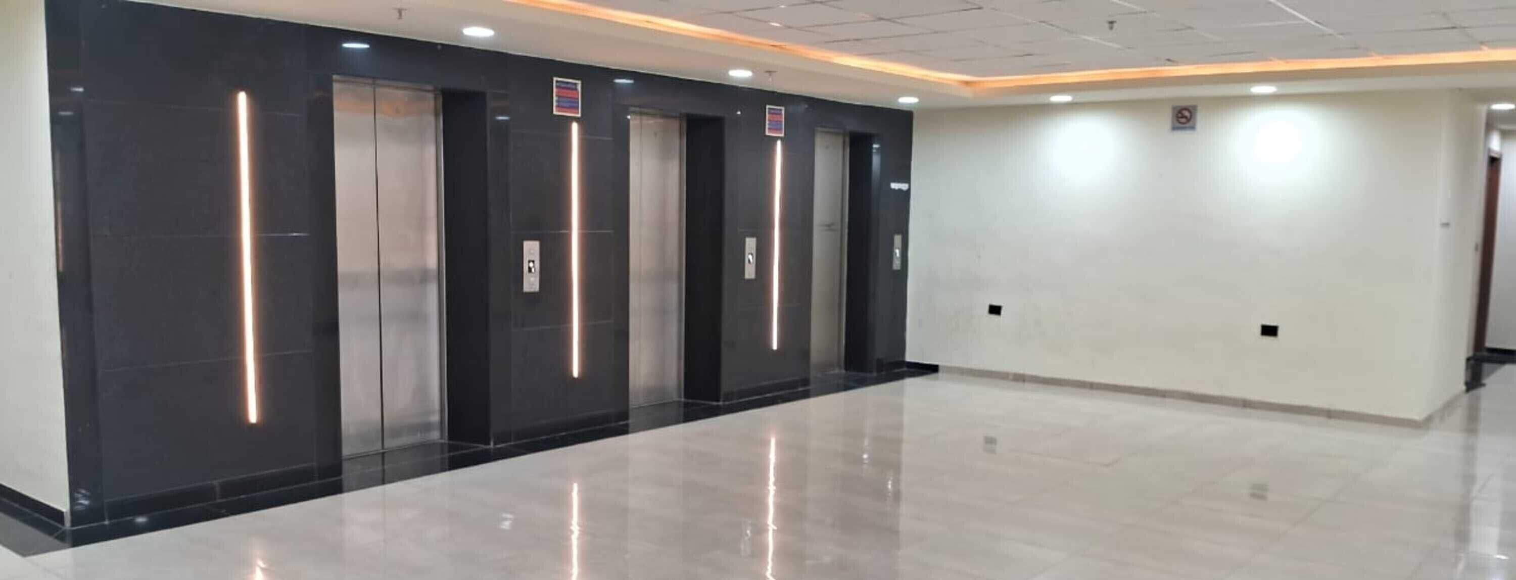 A modern elevator area with four elevators, each with a metallic finish and illuminated by vertical light strips.