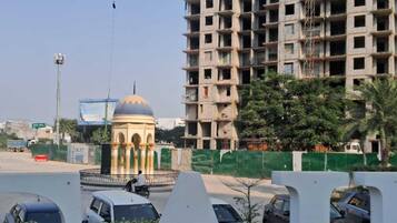 A view of a cityscape with a large, unfinished building, a roundabout, and parked cars.