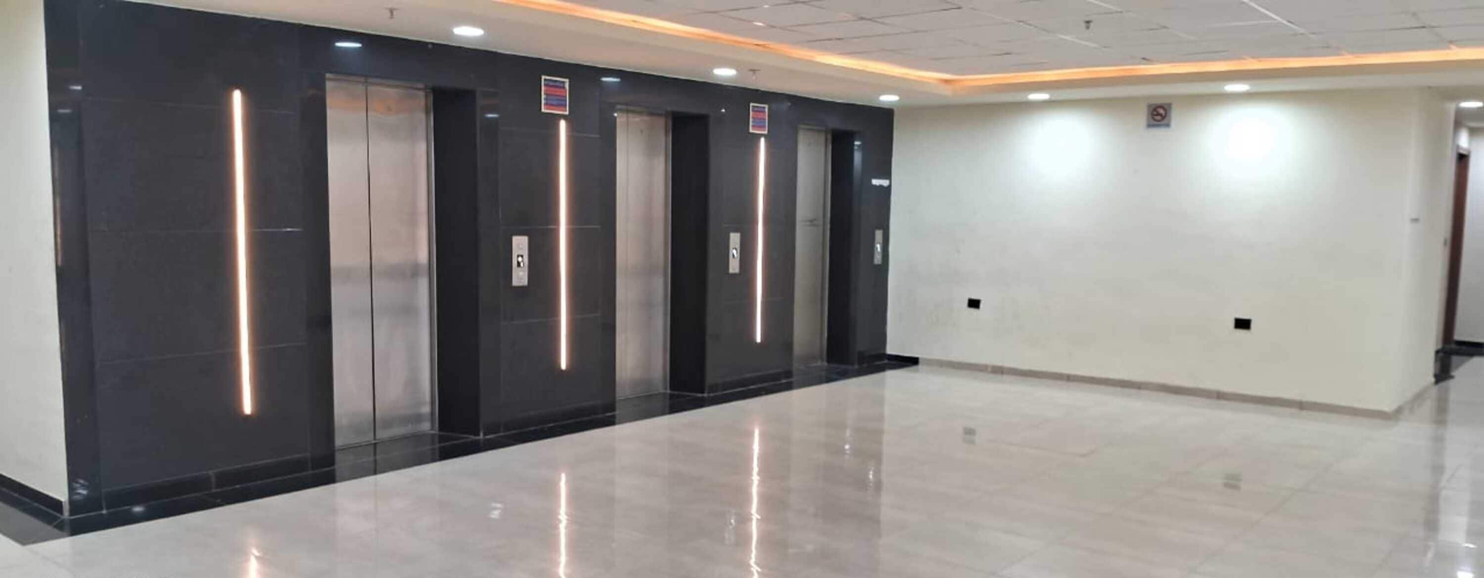 A modern elevator area with four elevators, a polished floor, and a plain wall with a no-smoking sign.
