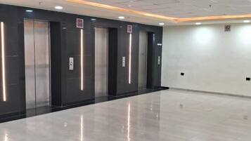 A modern elevator area with four elevators, a polished floor, and a plain wall with a no-smoking sign.