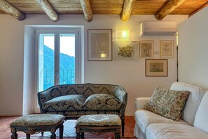 A room with a wooden ceiling, a sofa, a chair, and a window with a view of a mountain.