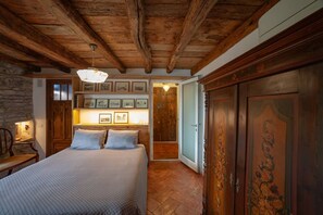 Quarto com teto de madeira, cama com colcha estampada, quadros nas paredes e guarda-roupa de madeira.