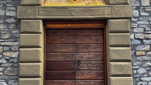 Une porte en bois munie d’un loquet métallique, encadrée par un mur de pierre sur lequel est fixée une plaque décorative.