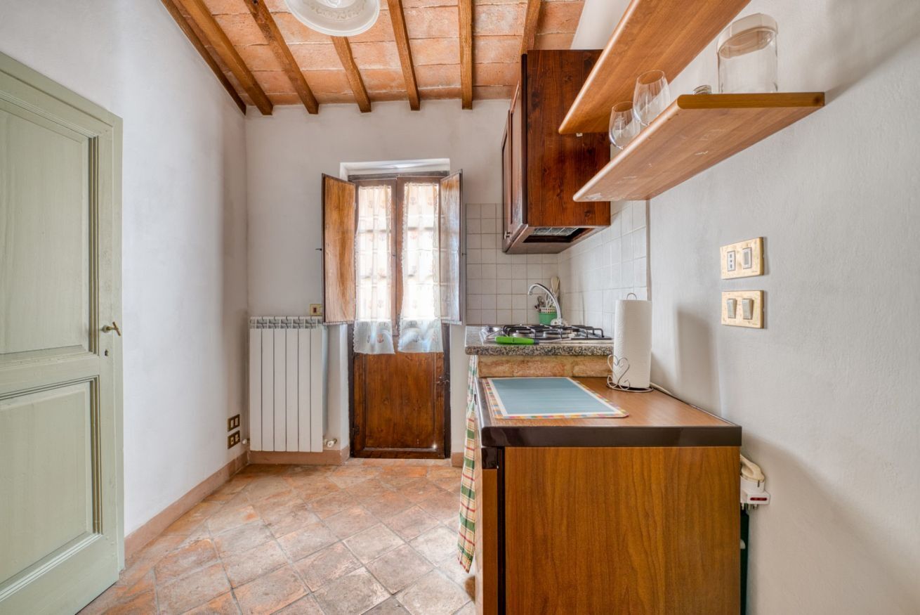 A compact kitchen with a wooden ceiling, a window, a radiator, and a countertop with a sink.