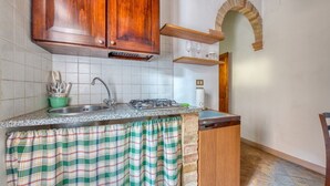 Una cocina con armarios de madera, salpicadero azulejado, pileta de acero inoxidable, estufa a gas y cortina a rayas verde y blanca.