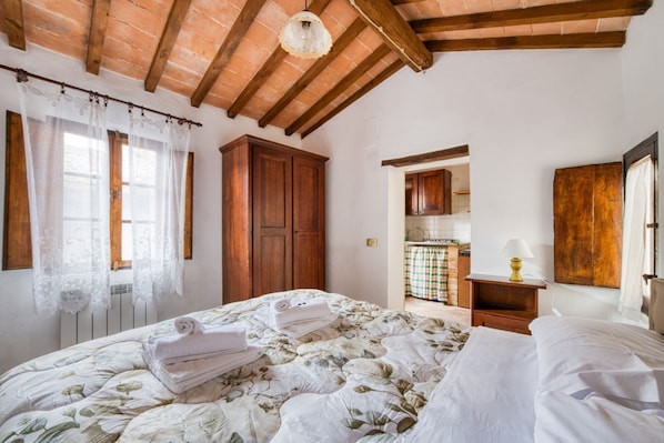 A bedroom with a bed, wooden wardrobe, and a small kitchen area.