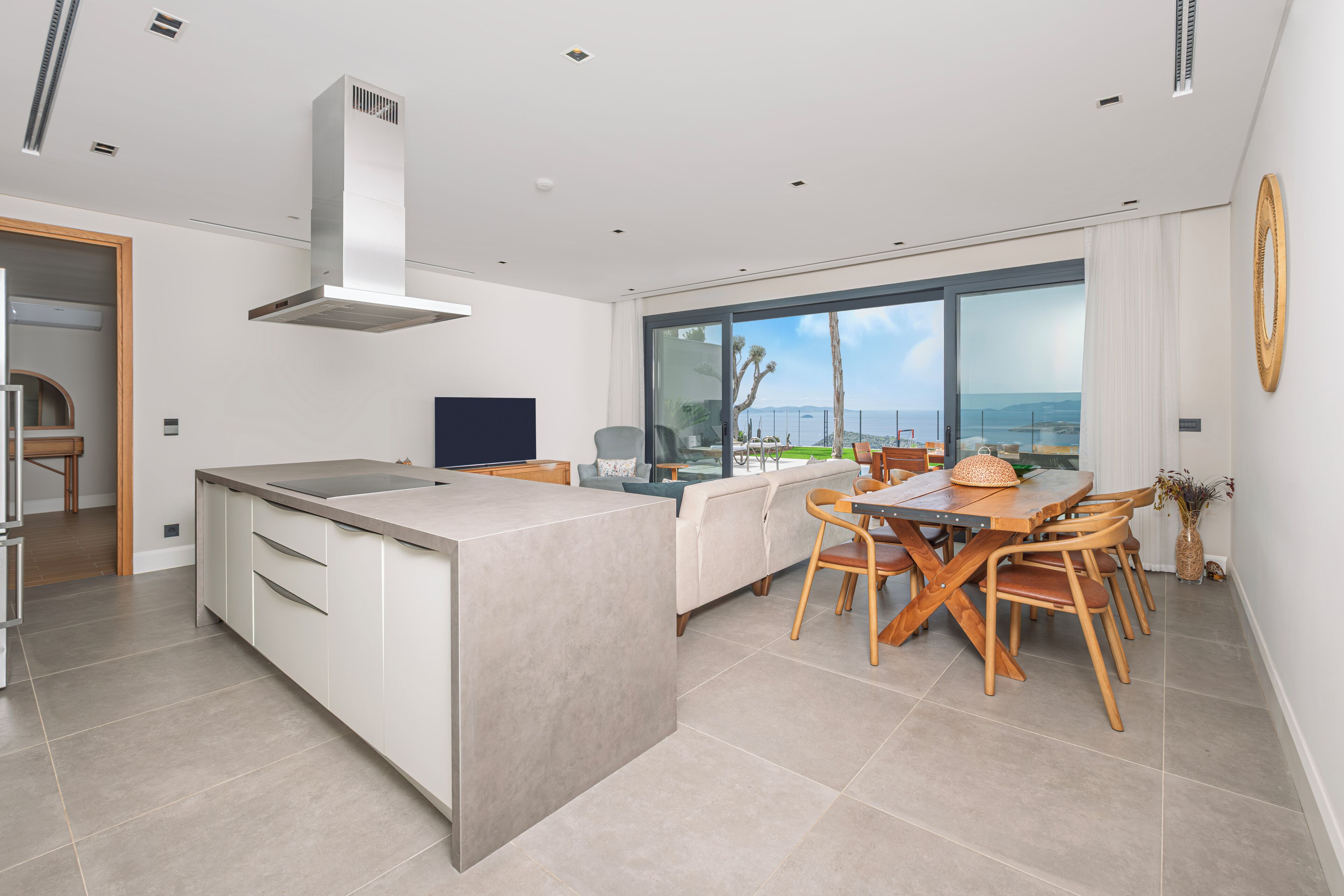 Una cocina moderna con una isla grande, un comedor con sillas de madera y vistas al océano a través de amplios ventanales.