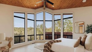 A bedroom with a large bed, a ceiling fan, and a view of the outdoors through large windows. - Luxury by Nature - Sedona Designer Retreat (Sedona)