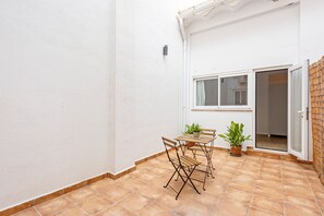 A patio with a table and chairs, a potted plant, and a sliding glass door leading to an interior space.