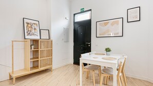 Ein Zimmer mit einem weißen Tisch, Stühlen, einer schwarzen Tür und gerahmten Kunstwerken an den Wänden.