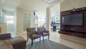 Ein geräumiges Wohnzimmer mit einem großen Flachbildfernseher an einer Holzwand, zwei Sessel und einem gemusterten Teppich.
