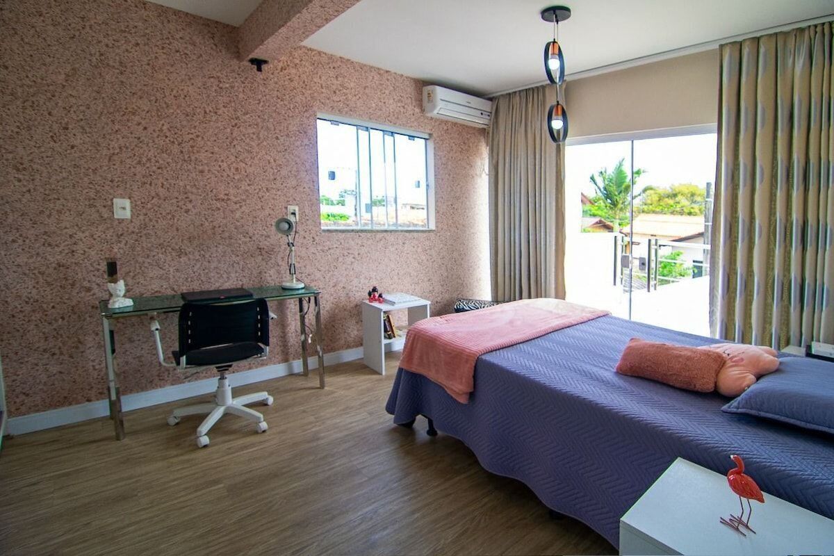 A hotel room with a large bed, a desk with a chair, a small table, and a window with curtains.