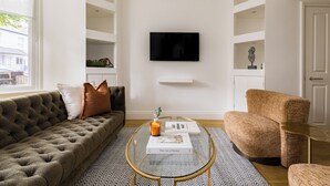 Una sala de estar moderna con un sofá capitonado, una mesa redonda de centro y un televisor montado en la pared.