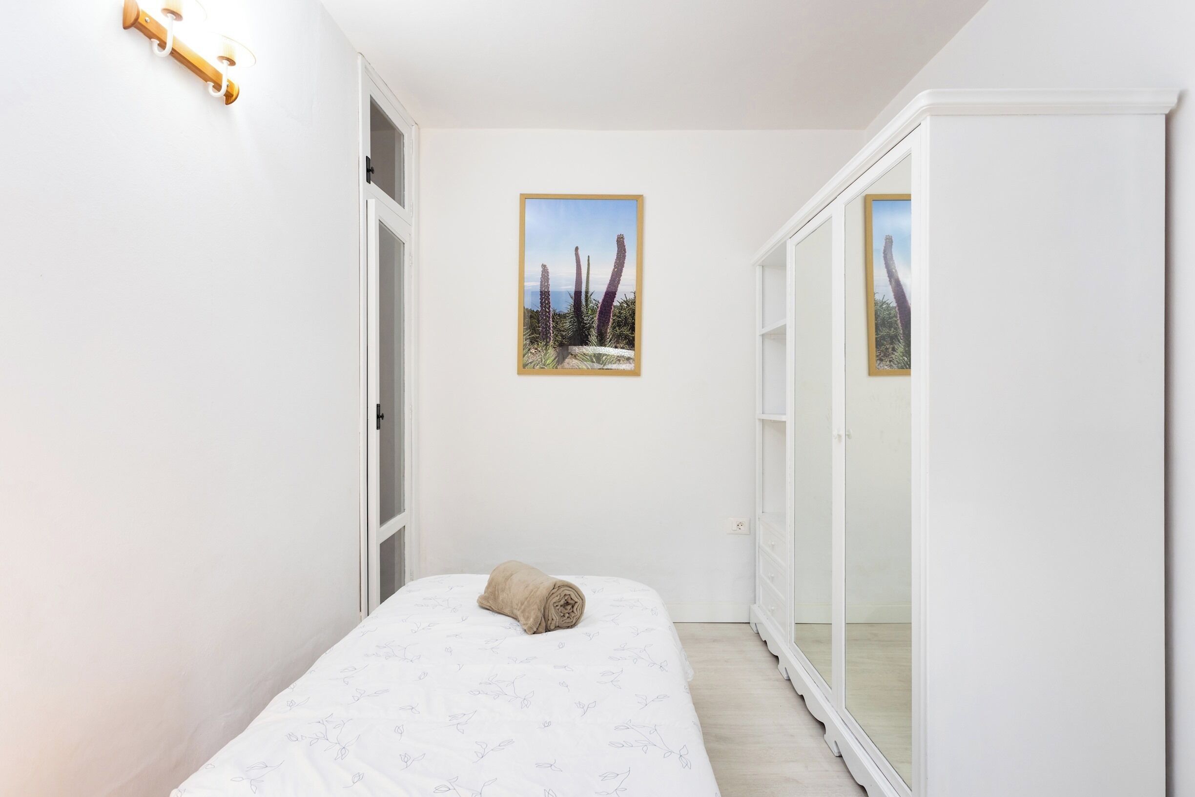 A bedroom with a bed, a rolled towel, a framed cactus picture, and a sliding door.