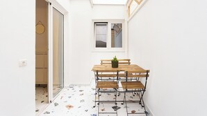 A small, bright room with a wooden table and benches, a potted plant, and a window.